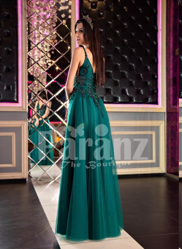 Woman’s stylish deep green evening gown with side slit tulle skirt and rich rhinestone bodice back side view